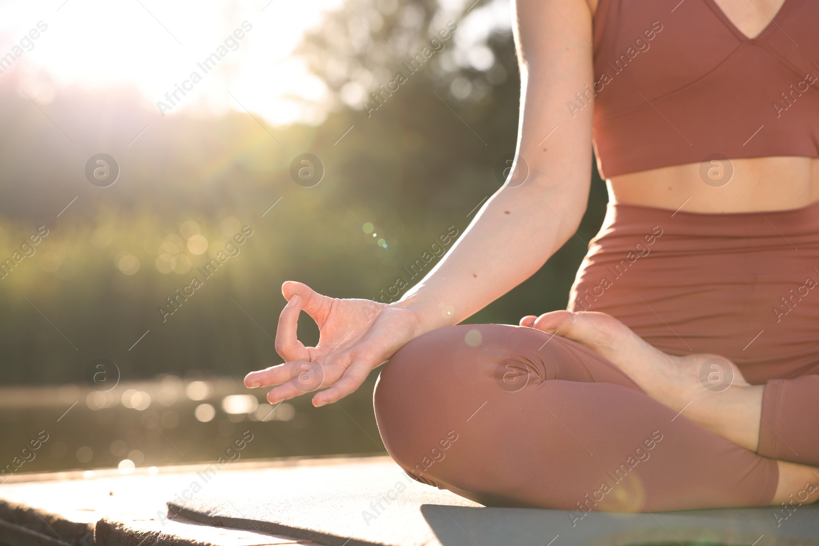 Photo of Woman practicing Padmasana on yoga mat on wooden pier near pond, closeup with space for text. Lotus pose