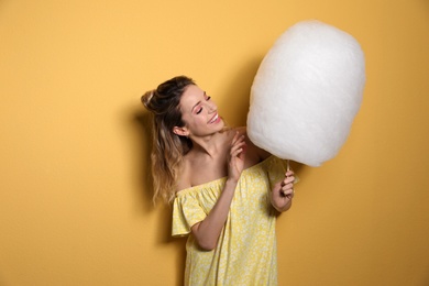 Portrait of young woman with cotton candy on yellow background