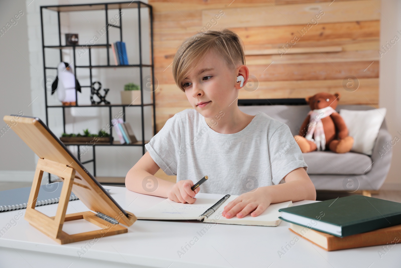 Photo of Boy in earphones doing homework with tablet at table indoors