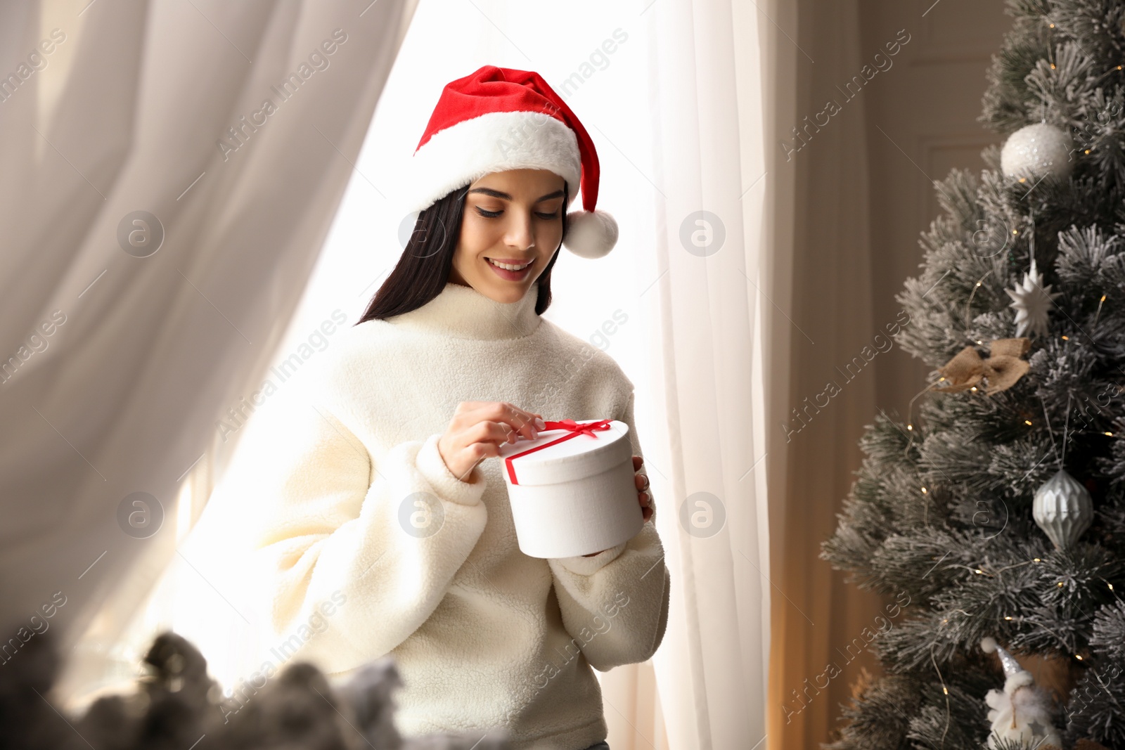 Photo of Woman in Santa hat opening gift box near Christmas tree