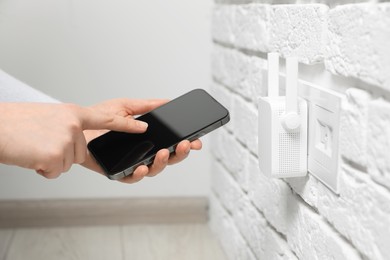 Woman using smartphone for wireless Wi-Fi repeater indoors, closeup