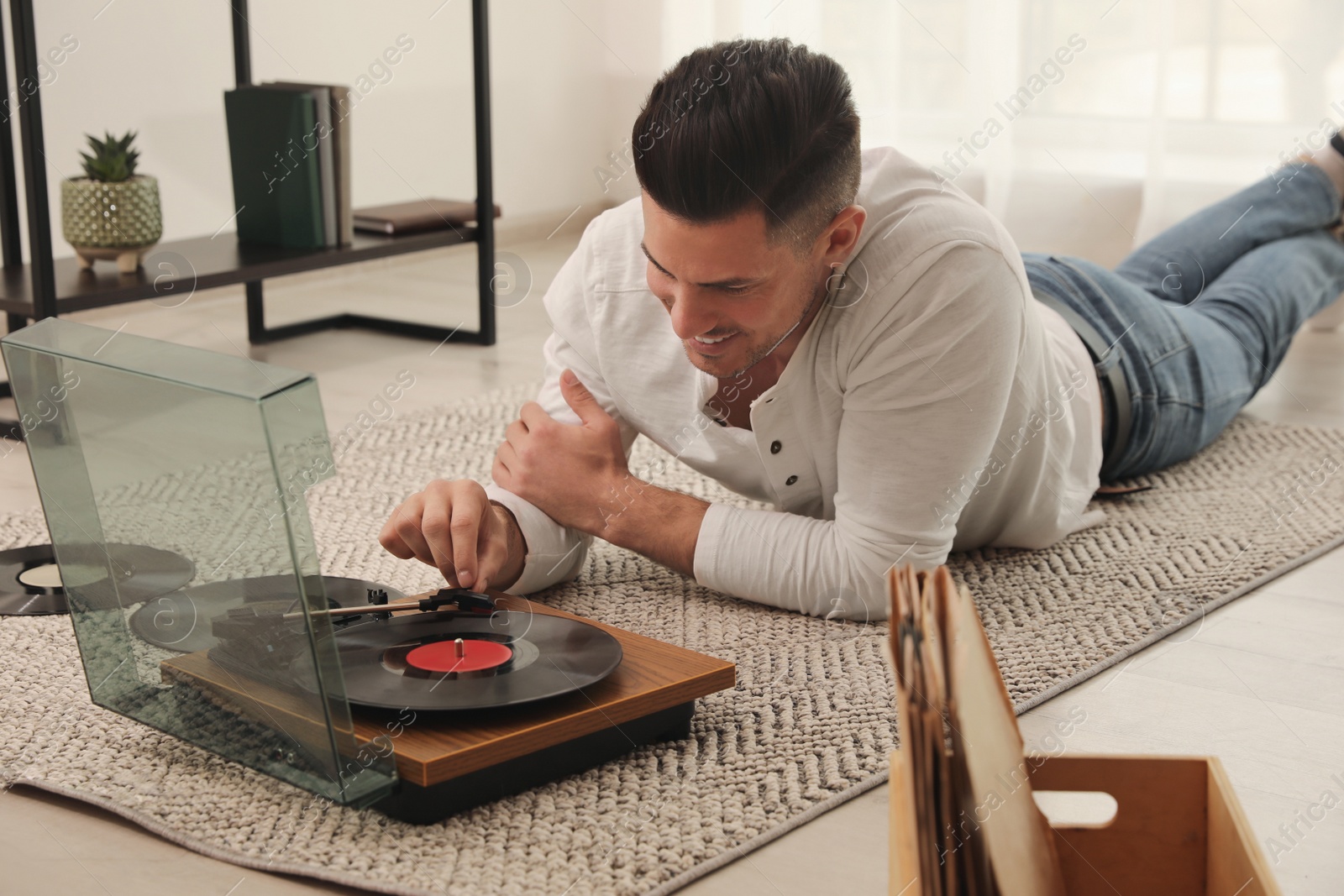 Photo of Happy man using turntable while lying on floor at home