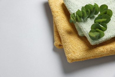 Photo of Soft folded towels with eucalyptus branches on light grey background. Space for text