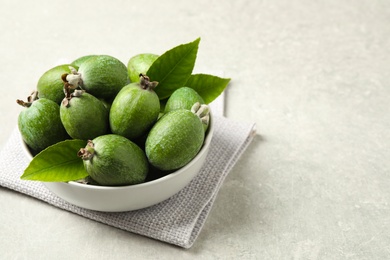 Photo of Delicious fresh feijoas in bowl on light grey table. Space for text