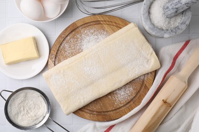 Photo of Raw puff pastry dough and ingredients on white tiled table, flat lay