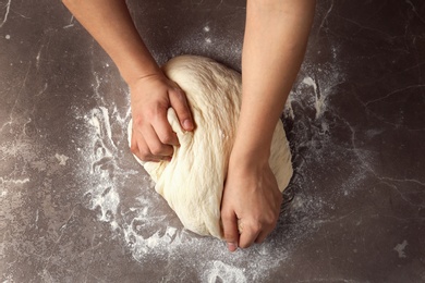 Photo of Female baker preparing bread dough at grey table, top view