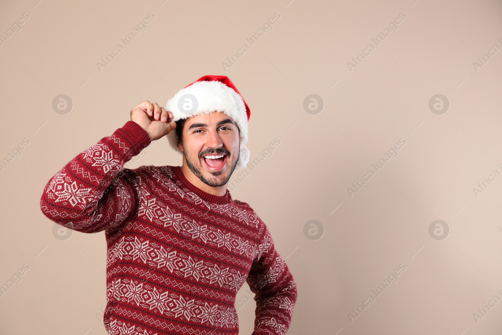 Photo of Portrait of young man in Christmas sweater and Santa hat on beige background