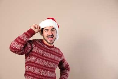 Portrait of young man in Christmas sweater and Santa hat on beige background