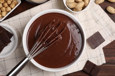 Bowl of chocolate cream with whisk and nuts on wooden table, flat lay