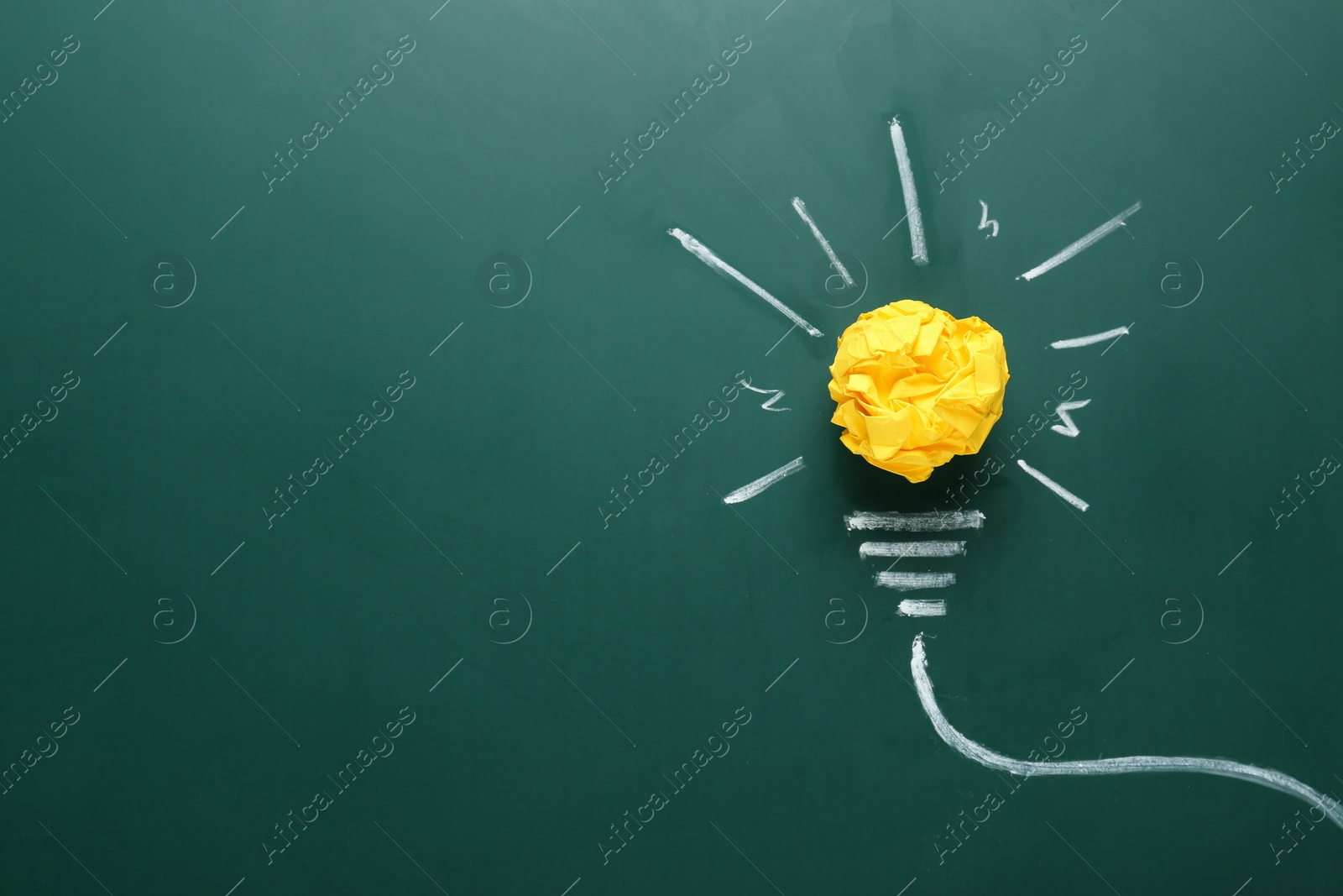 Photo of Composition with crumpled paper ball and drawing of lamp bulb on green chalkboard, top view. Idea concept