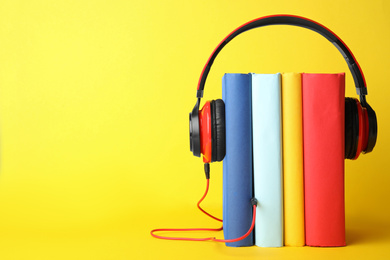 Photo of Books with modern headphones on yellow background. Space for text