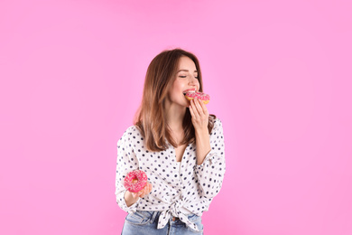 Beautiful young woman with donuts on light pink background