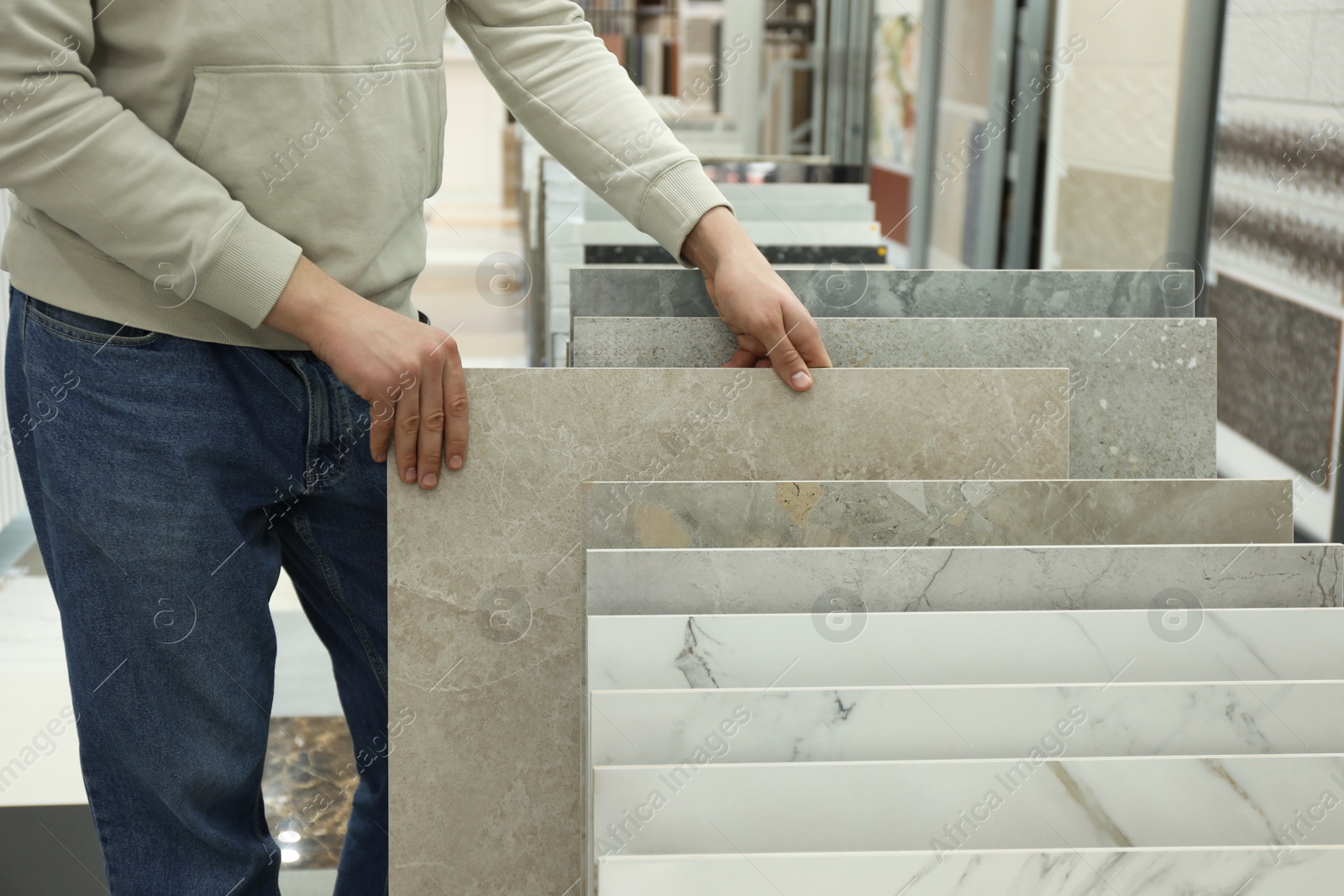 Photo of Man choosing tile among different samples in store, closeup