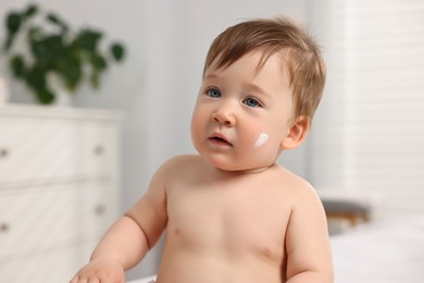 Cute little baby with moisturizing cream on face indoors