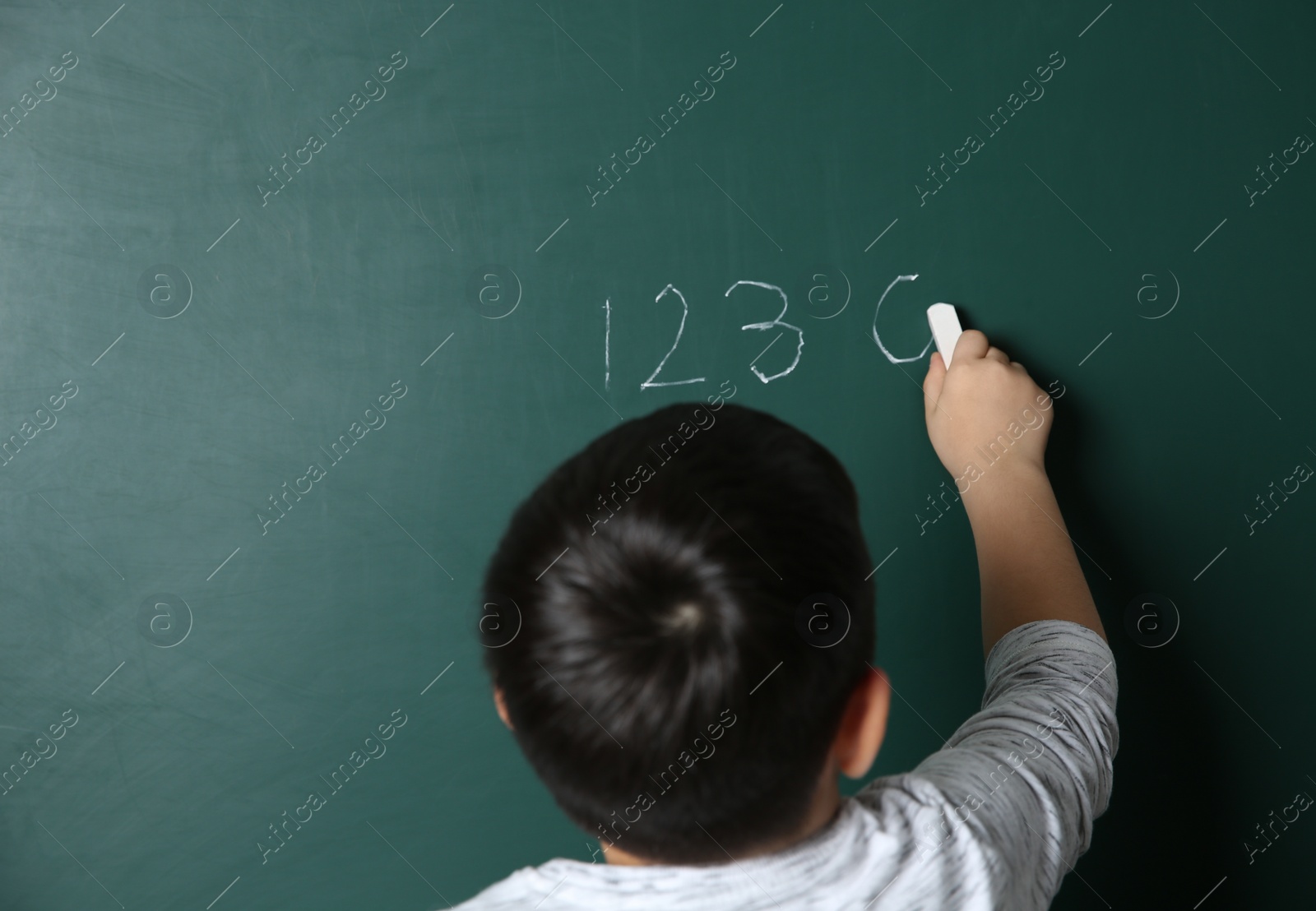 Photo of Child writing math sum on chalkboard. Space for text