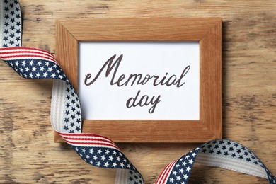 Photo of Frame with phrase Memorial Day and ribbon on wooden table, flat lay