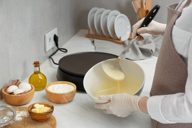 Woman cooking delicious crepe at white marble table in kitchen, closeup