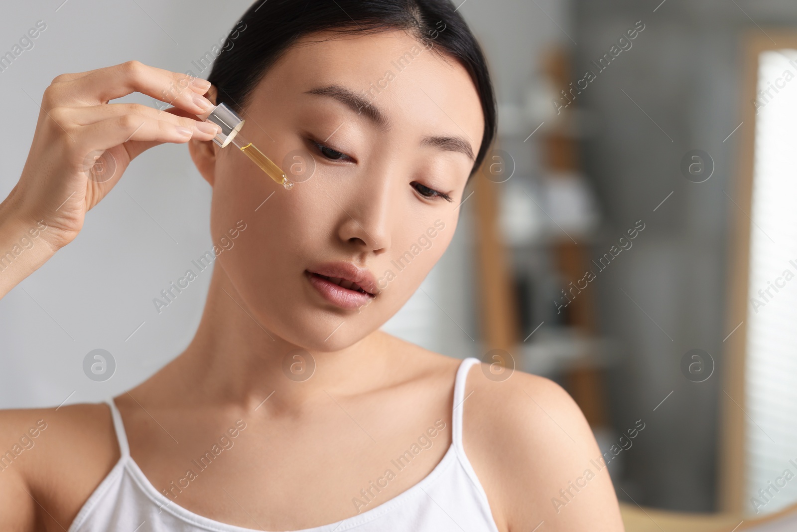 Photo of Beautiful young woman applying cosmetic serum onto her face in bathroom, closeup. Space for text