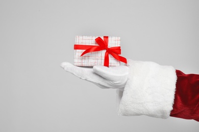 Photo of Santa Claus holding Christmas gift on light grey background, closeup of hand