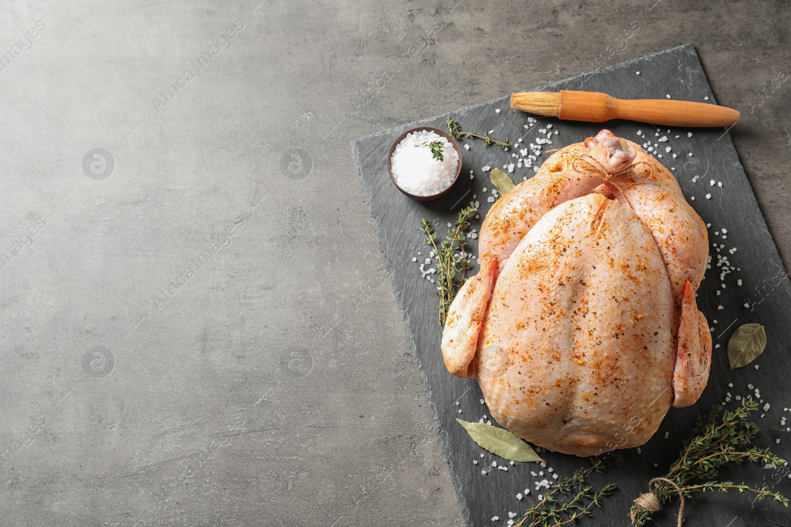 Photo of Slate plate with raw spiced turkey on grey background, top view. Space for text