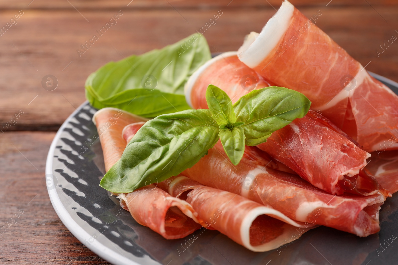 Photo of Plate with rolled slices of delicious jamon and basil on wooden table, closeup