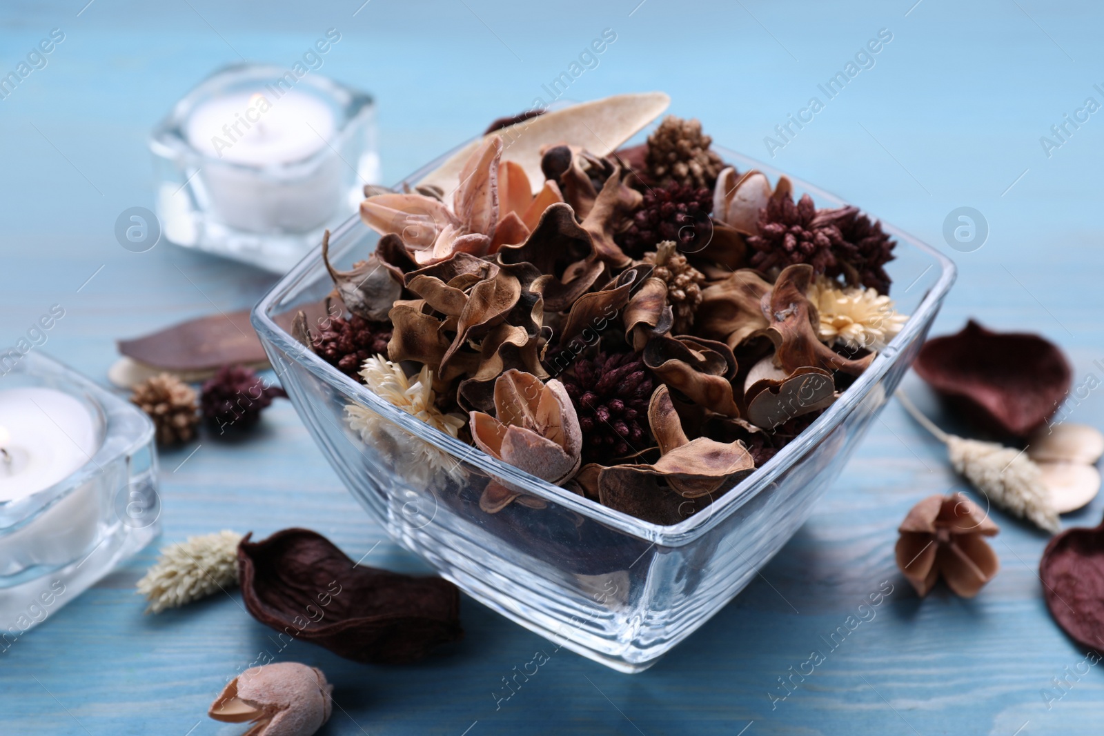 Photo of Aromatic potpourri of dried flowers in glass bowl on light blue wooden table