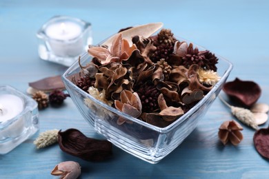 Photo of Aromatic potpourri of dried flowers in glass bowl on light blue wooden table