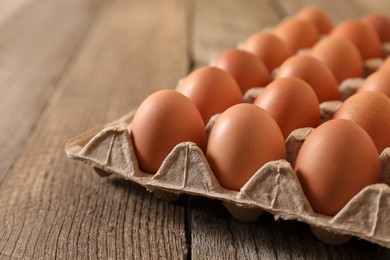 Fresh raw chicken eggs in carton on wooden table, closeup