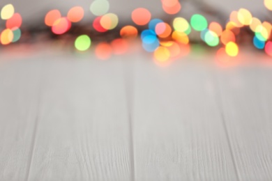 Colorful lights on light wooden table, blurred view. Space for text
