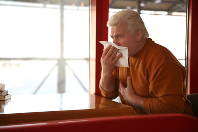 Photo of Sick senior man with tissue in cafe. Influenza virus