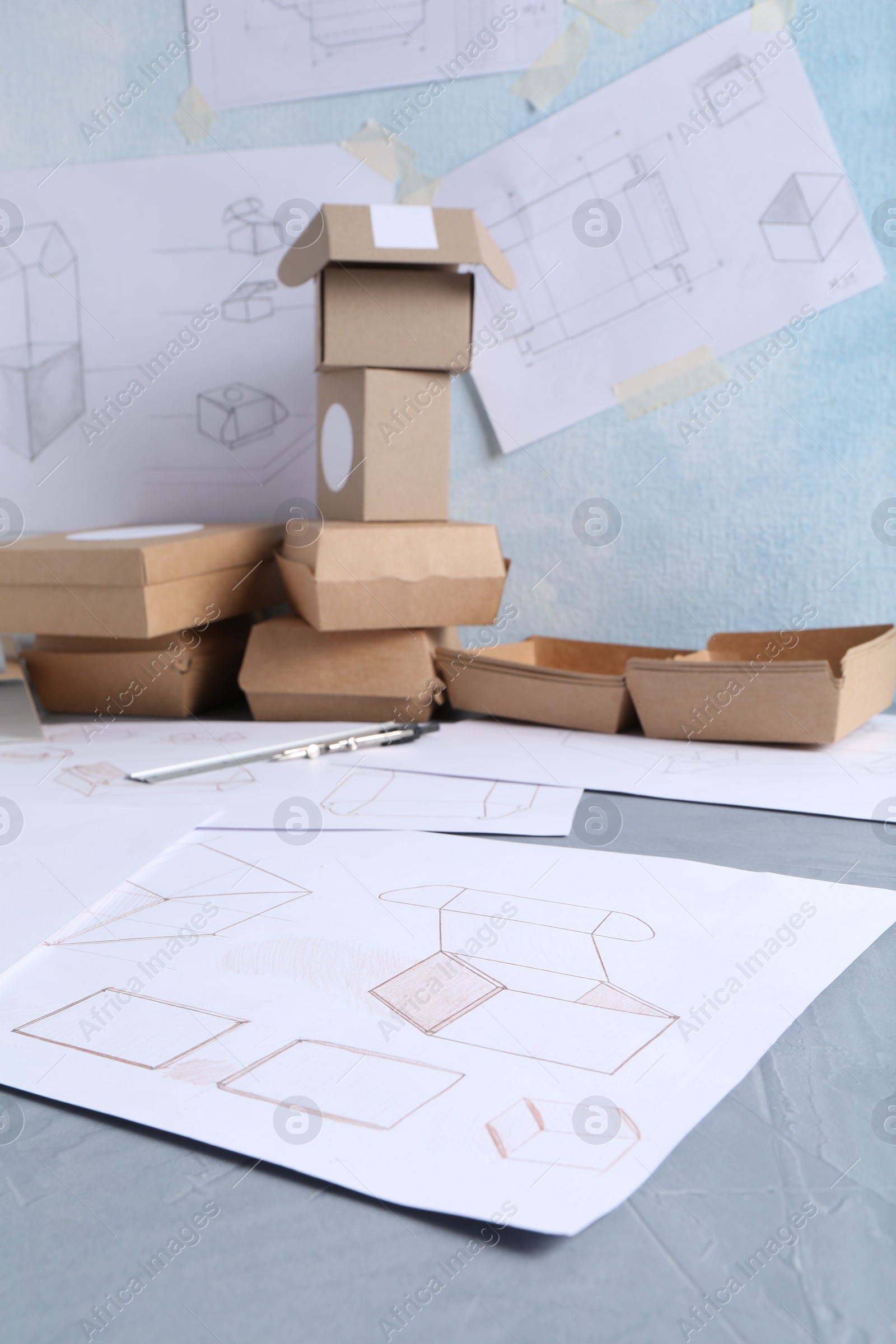 Photo of Creating packaging design. Drawings and boxes on blue textured table, closeup