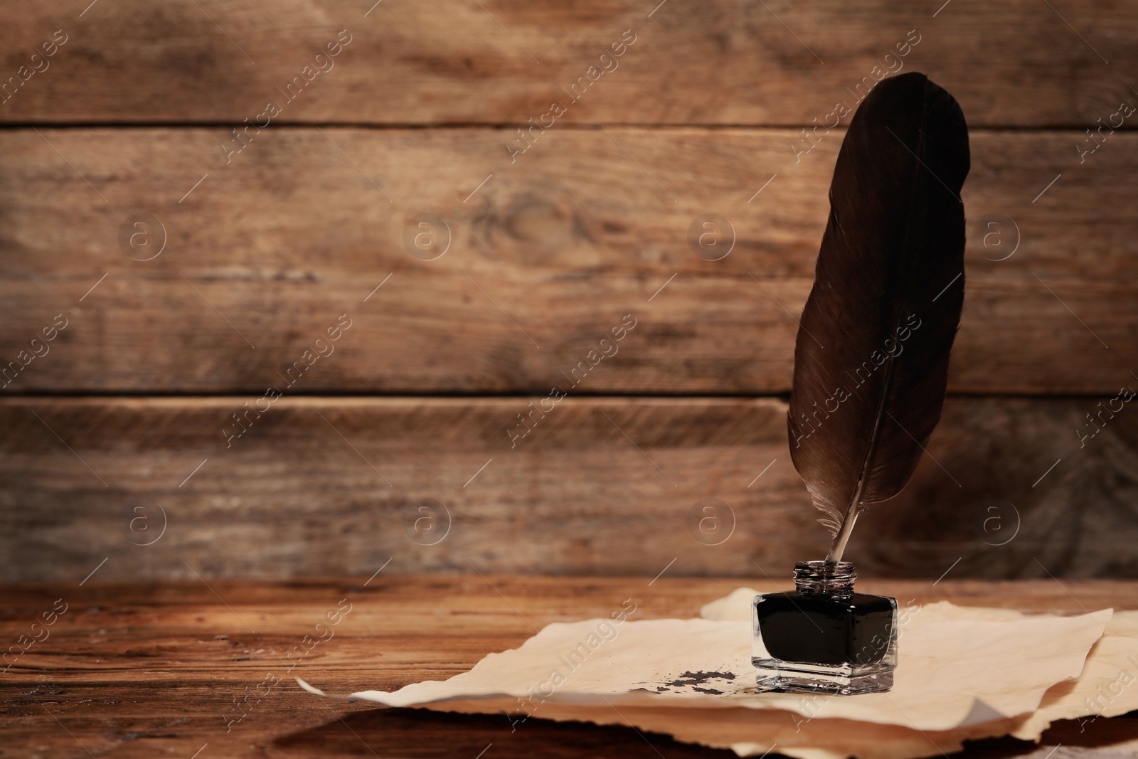 Photo of Inkwell with feather and vintage parchment with stains on wooden table. Space for text