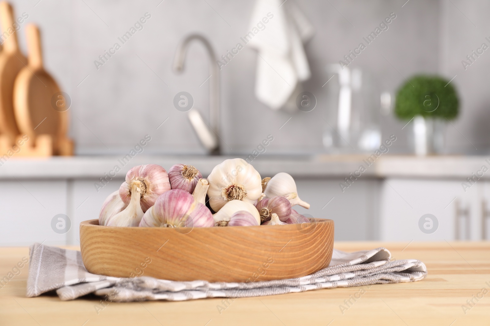 Photo of Bowl of fresh raw garlic on wooden table in kitchen, space for text