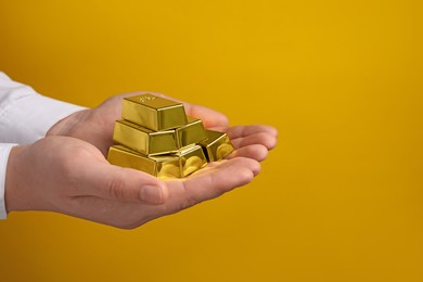 Photo of Woman holding many shiny gold bars on yellow background, closeup. Space for text