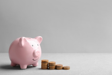 Photo of Piggy bank and coins on table against grey background. Space for text