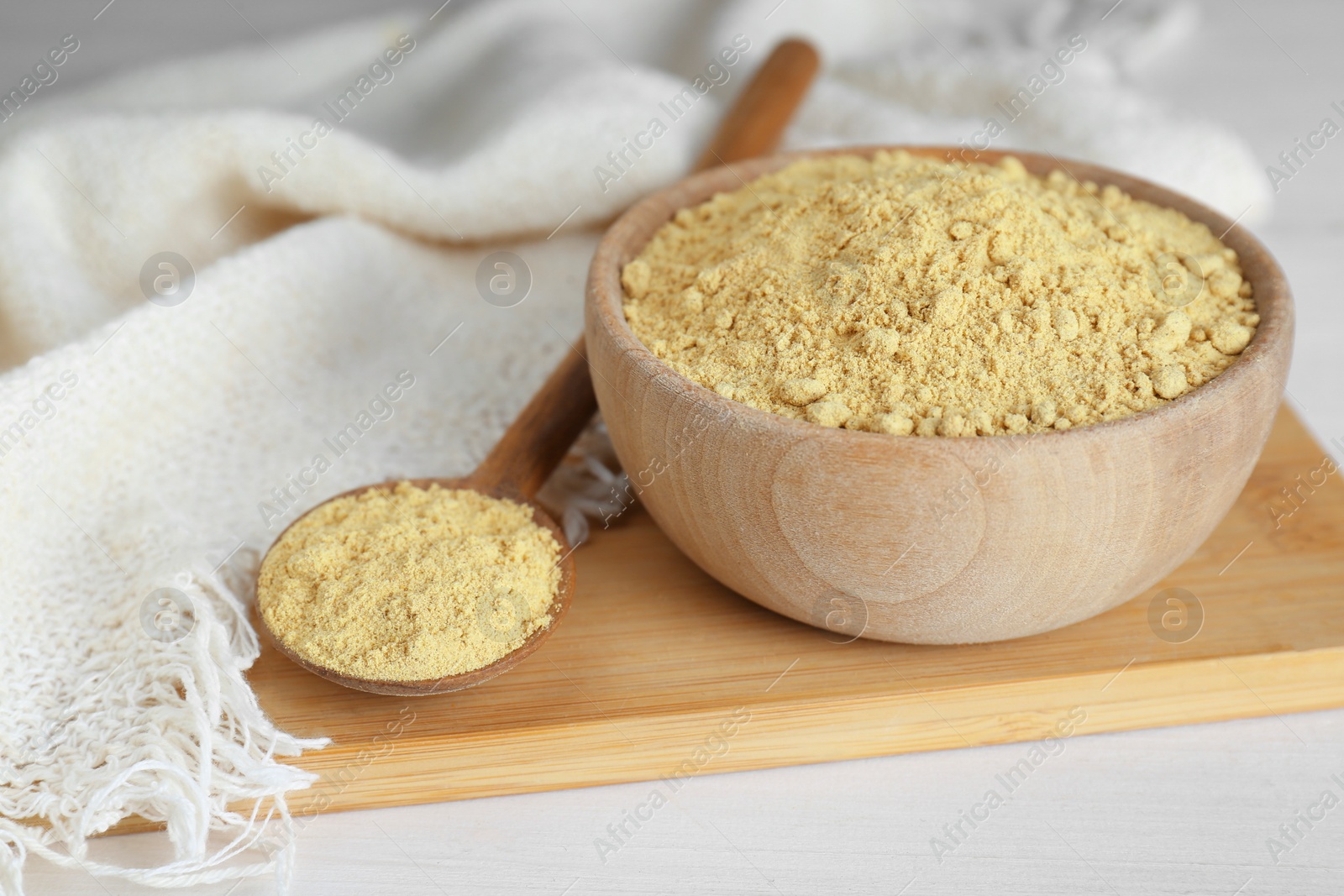 Photo of Bowl and spoon with aromatic mustard powder on white wooden table, closeup