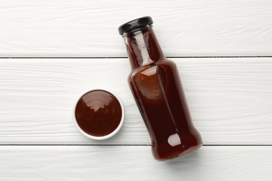 Photo of Tasty barbeque sauce in bottle and bowl on white wooden table, top view