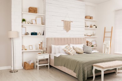 Photo of Stylish room interior with large comfortable bed, wall shelves and beautiful decor elements