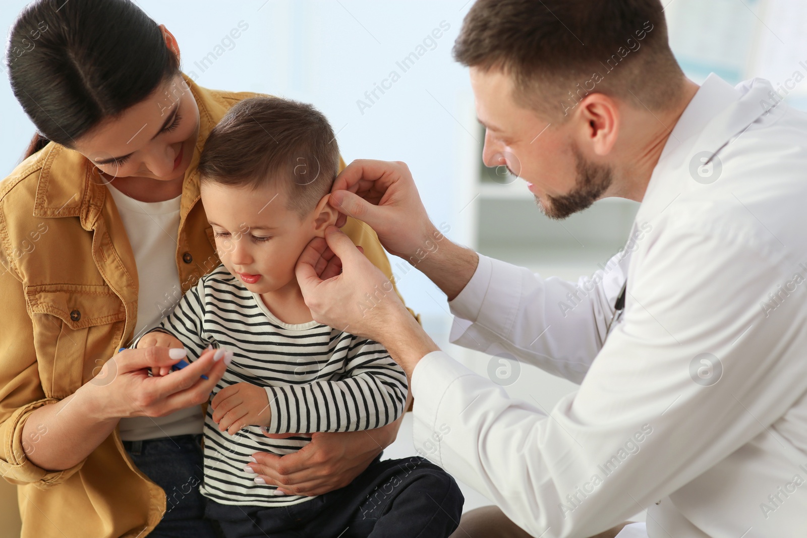 Photo of Mother and son visiting pediatrician in hospital. Doctor examining little boy