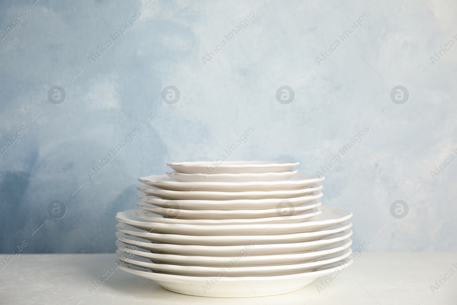 Photo of Stack of clean plates on table against light blue background. Space for text