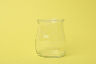 Open empty glass jar on light yellow background