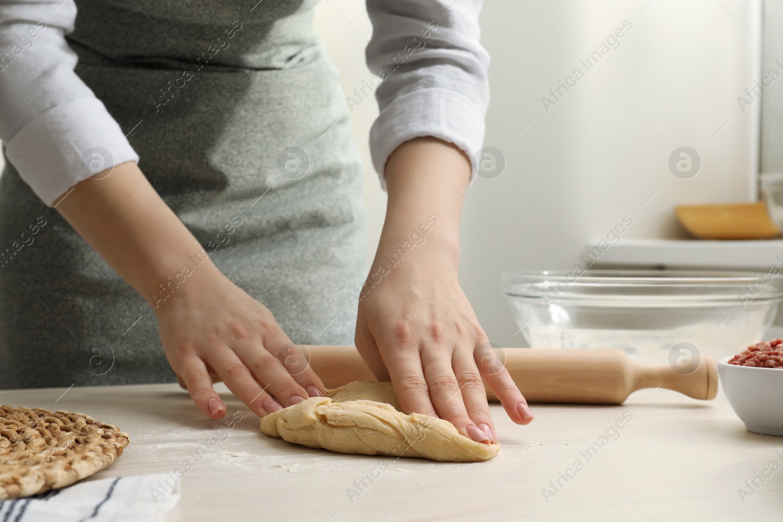 Photo of Woman kneading raw dough at white wooden table, closeup