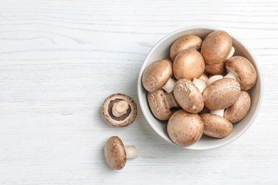 Photo of Bowl of fresh champignon mushrooms on wooden background, top view with space for text