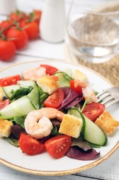 Photo of Tasty salad with croutons, tomato and shrimps served on white wooden table, closeup