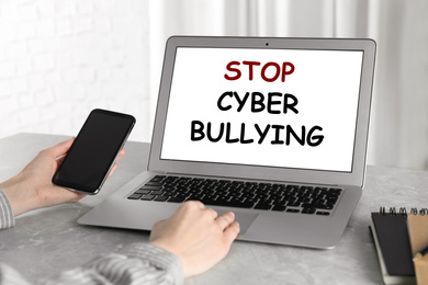 Young woman using laptop at grey marble table, closeup. Cyber bullying