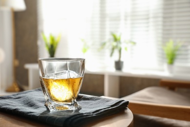 Glass of whiskey on wooden table in modern room interior, space for text