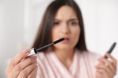 Photo of Beautiful woman holding mascara brush with fallen eyelashes indoors, closeup