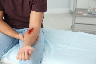 Photo of Young man with injured arm in clinic, space for text. First aid