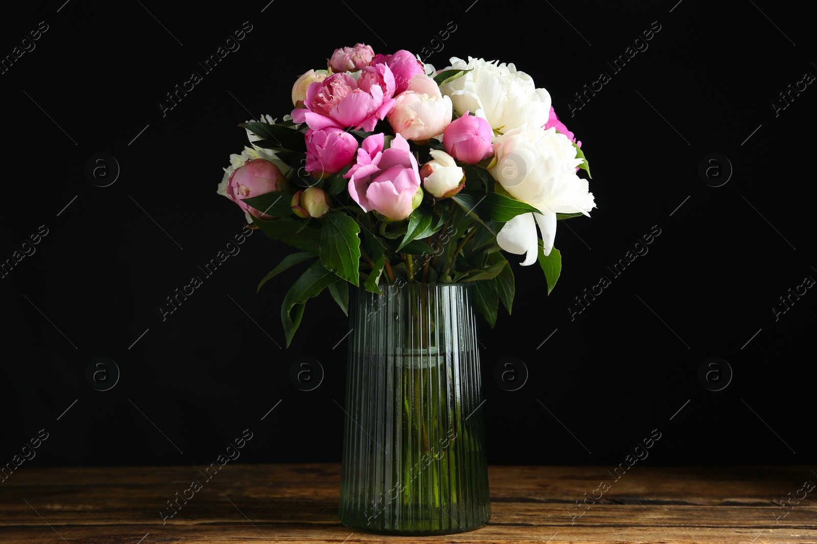 Photo of Bouquet of beautiful peonies in vase on wooden table against black background