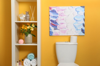 Shelves with different stuff above toilet bowl near orange wall in restroom interior